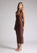 Front quarter image of a blonde model wearing a chocolate midaxi dress with a halter neckline, sleeveless, and a back skirt split. The design features is the Vesper Asher Chocolate Halter Neck Midaxi Dress