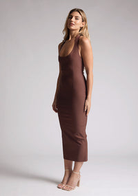 Front quarter image of a blonde model wearing a chocolate midaxi dress with a halter neckline, sleeveless, and a back skirt split. The design features is the Vesper Asher Chocolate Halter Neck Midaxi Dress