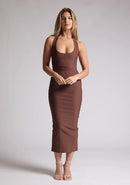 Front image of a blonde model wearing a chocolate midaxi dress with a halter neckline, sleeveless, and a back skirt split. The design features is the Vesper Asher Chocolate Halter Neck Midaxi Dress