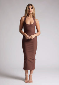 Front image of a blonde model wearing a chocolate midaxi dress with a halter neckline, sleeveless, and a back skirt split. The design features is the Vesper Asher Chocolate Halter Neck Midaxi Dress