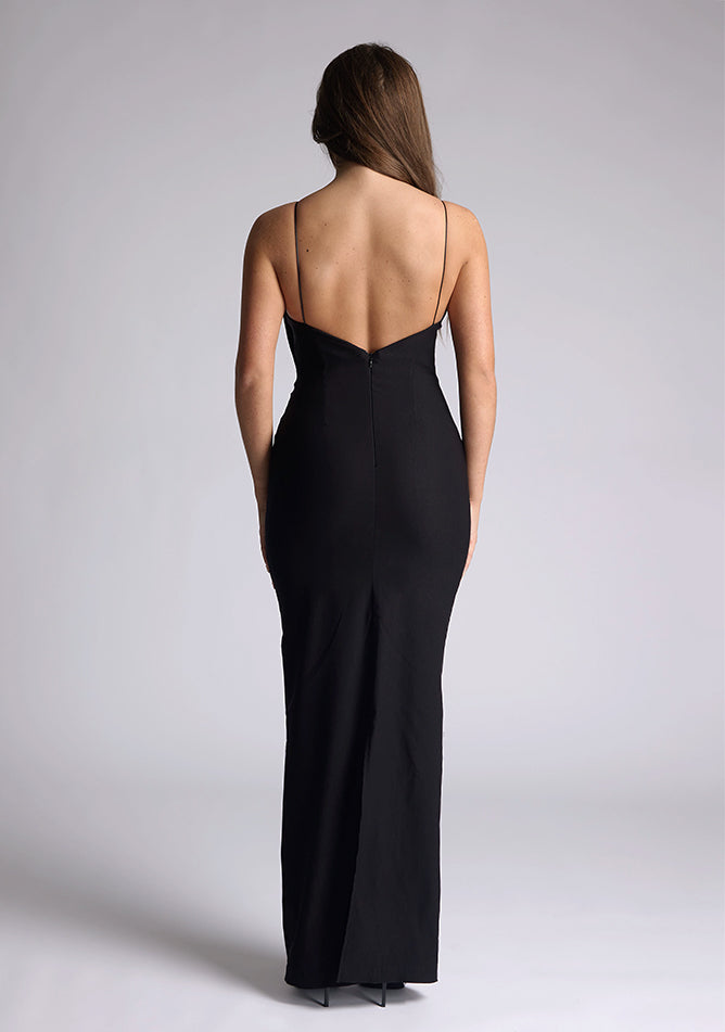 Back image of a of a model wearing a black maxi dress with a plunge neckline and bow detailing. The design featured is the Vesper Bellini Black Bow Maxi Dress
