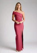 Front image of model wearing a raspberry maxi dress with a stunning one-sleeve off-shoulder design and an alluring front skirt split. The design featured is the Vesper Carmel Raspberry Maxi Dress