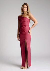 Front quarter image of model wearing a raspberry maxi dress with a stunning one-sleeve off-shoulder design and an alluring front skirt split. The design featured is the Vesper Carmel Raspberry Maxi Dress