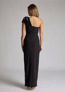Back image of blonde model wearing an Black One Shoulder Maxi Dress with a asymmetric neckline, bodycon fit, front skirt split and a graceful shoulder ribbon tie, dress featured is Vesper Ceylon Black One Shoulder Maxi Dress