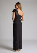 Back quarter image of blonde model wearing an black one shoulder maxi dress with a asymmetric neckline, bodycon fit, front skirt split and a graceful shoulder ribbon tie, dress featured is Vesper Ceylon Black One Shoulder Maxi Dress