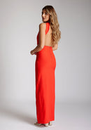 Back quarter image of a model wearing a red maxi dress with a asymmetric neckline, with an open back and an asymmetric statement strap across the back and front skirt split. The designe featured is Vesper Deva Red Maxi Dress