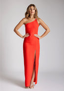 Front image of a model wearing a red maxi dress with a asymmetric neckline, with an open back and an asymmetric statement strap across the back and front skirt split. The designe featured is Vesper Deva Red Maxi Dress