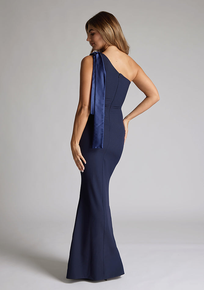 Back quarter image of a blonde model wearing a Navy Maxi Dress with an asymmetric neckline and one-shoulder, design features Vesper Deven Navy Fishtail Maxi Dress