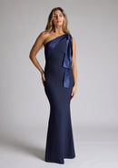 Front image of a blonde model wearing a Navy Maxi Dress with an asymmetric neckline and one-shoulder, design features Vesper Deven Navy Fishtail Maxi Dress