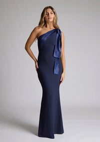 Front image of a blonde model wearing a Navy Maxi Dress with an asymmetric neckline and one-shoulder, design features Vesper Deven Navy Fishtail Maxi Dress