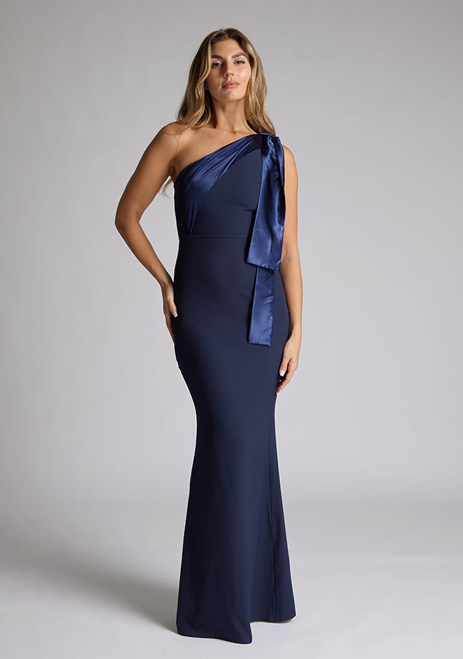 Front image of a blonde model wearing a Navy Maxi Dress with an asymmetric neckline and one-shoulder, design features Vesper Deven Navy Fishtail Maxi Dress