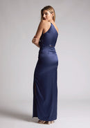 Back quarter image of a model wearing a navy satin maxi dress with a asymmetric neckline, one shoulder detail, side waist cut-out and a side skirt split. The design featured is the Vesper Esme Navy Satin  Maxi Dress