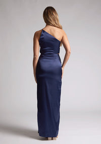Back image of a model wearing a navy satin maxi dress with a asymmetric neckline, one shoulder detail, side waist cut-out and a side skirt split. The design featured is the Vesper Esme Navy Satin  Maxi Dress