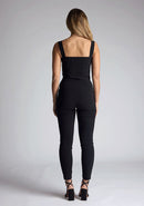 Back image of the model wearing pine green top with a sweetheart neckline and wide straps create a flattering silhouette, while the circular cut outs at the hem add a touch of edge and statement front zip. The design featured is the Vesper Juno Black Crop Top paired with Vesper Raven Black High Waist Trousers