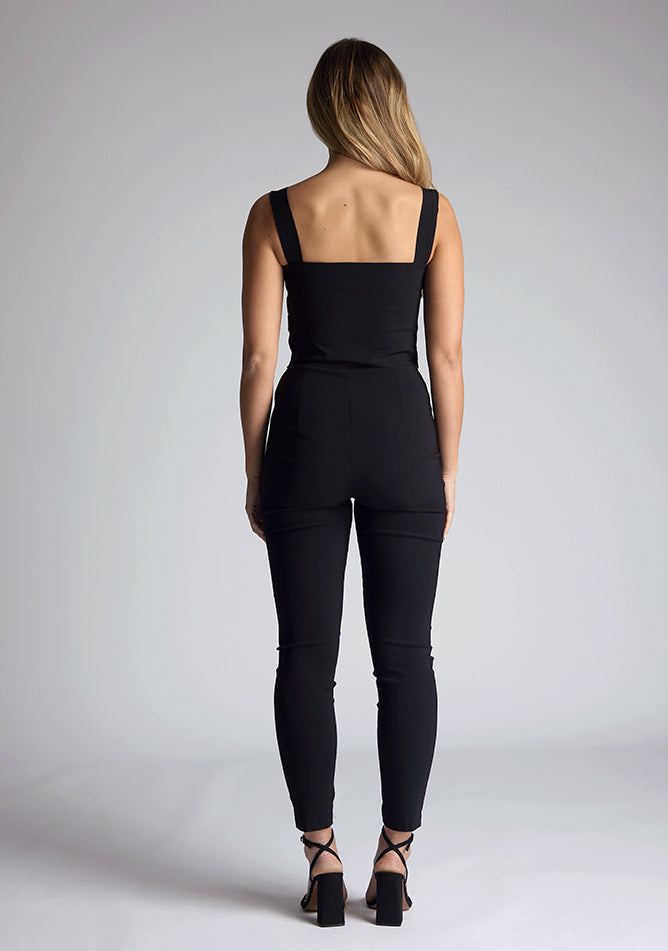 Back image of the model wearing pine green top with a sweetheart neckline and wide straps create a flattering silhouette, while the circular cut outs at the hem add a touch of edge and statement front zip. The design featured is the Vesper Juno Black Crop Top paired with Vesper Raven Black High Waist Trousers
