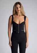 Close up image of the model wearing pine green top with a sweetheart neckline and wide straps create a flattering silhouette, while the circular cut outs at the hem add a touch of edge and statement front zip. The design featured is the Vesper Juno Black Crop Top paired with Vesper Raven Black High Waist Trousers