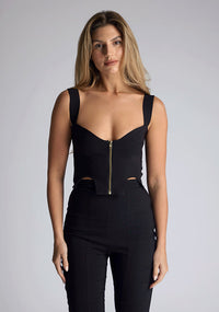 Close up image of the model wearing pine green top with a sweetheart neckline and wide straps create a flattering silhouette, while the circular cut outs at the hem add a touch of edge and statement front zip. The design featured is the Vesper Juno Black Crop Top paired with Vesper Raven Black High Waist Trousers