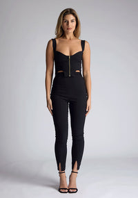 Front image of the model wearing pine green top with a sweetheart neckline and wide straps create a flattering silhouette, while the circular cut outs at the hem add a touch of edge and statement front zip. The design featured is the Vesper Juno Black Crop Top paired with Vesper Raven Black High Waist Trousers