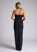 Back image of blonde model wearing a black maxi dress with a  features a sweetheart neckline, centre back zip and a side skirt split. The design featured is the Vesper Larissa Black Bodycon Maxi Dress