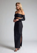 Front quarter image of a blonde model wearing a black maxi dress with a strapless design, off-shoulder design, and a stylish side cut-out, the design features Vesper Leena Black Maxi Dress