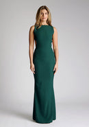 Front image of a model wearing a green maxi dress, featuring a slash neckline, open back, subtle fishtail skirt and gold buttons at back of neck. The style featured is Vesper Lincoln Forest Green Maxi Dress