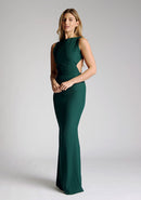 Front quarter image of a model wearing a green maxi dress, featuring a slash neckline, open back, subtle fishtail skirt and gold buttons at back of neck. The style featured is Vesper Lincoln Forest Green Maxi Dress