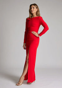 Front quarter image of a model wearing a red maxi dress with long sleeves, front skirt split and a low back. The design featured is the Vesper Mandy Red Long Sleeve Maxi Dress