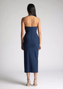 Back image of a model wearing a Navy Midaxi Dress with a halter neckline with a button fastening at the back, a front skirt split, and a center back zip, The design features a model wearing a Vesper Maria Navy Halter Midaxi Dress