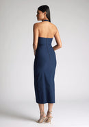 Back quarter image of a model wearing a Navy Midaxi Dress with a halter neckline with a button fastening at the back, a front skirt split, and a center back zip, The design features a model wearing a Vesper Maria Navy Halter Midaxi Dress
