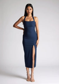Front image of a model wearing a Navy Midaxi Dress with a halter neckline with a button fastening at the back, a front skirt split, and a center back zip, The design features a model wearing a Vesper Maria Navy Halter Midaxi Dress
