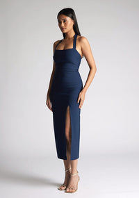 Front quarter image of a model wearing a Navy Midaxi Dress with a halter neckline with a button fastening at the back, a front skirt split, and a center back zip, The design features a model wearing a Vesper Maria Navy Halter Midaxi Dress
