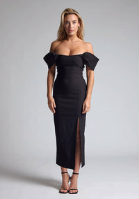 Front image of blonde model wearing a Black Midaxi Dress with a off-shoulder design, a flattering body-con sillhoutte, and a front skirt split,. The design features is the Vesper Marriot Black Bardot Midaxi Dress