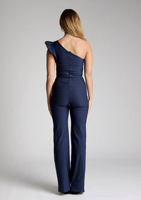 Back image of the model wearing a navy one shoulder jumpsuit
with a asymmetric neckline and one shoulder with a ruffle detail and wide leg finish elongates your silhouette, while the centre back zip ensures a sleek fit. The design featured is the Vesper Monty Navy One Shoulder Jumpsuit