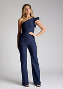 Front image of the model wearing a navy one shoulder jumpsuit with a asymmetric neckline and one shoulder with a ruffle detail and wide leg finish elongates your silhouette, while the centre back zip ensures a sleek fit. The design featured is the Vesper Monty Navy One Shoulder Jumpsuit