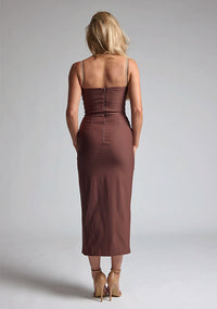Back image of a blonde model wearing a Chocolate Midaxi Dress with a daring plunge neckline, delicate thin straps, a flattering bodycon fit and a faux wrap skirt split adds a touch of sophistication to the overall design. The design features the Vesper Oaklynn Chocolate Midaxi Dress