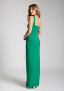 Back quarter image of a blonde model wearing a emerald green maxidress with a asymmetric neckline, front skirt split, and beautiful emerald green hue. The design featured is the Vesper Olivette Emerald Green Maxi Dress