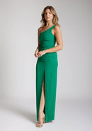Front quarter image of a blonde model wearing a emerald green maxidress with a asymmetric neckline, front skirt split, and beautiful emerald green hue. The design featured is the Vesper Olivette Emerald Green Maxi Dress