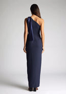 Back image of a model wearing a  One Shoulder Navy Maxi Dress with a  one shoulder contrast satin band and bow detail with a front skirt split. The design features Vesper Olympia One Shoulder Navy Maxi Dress