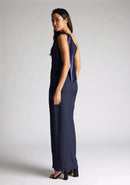 Back quarter image of a model wearing a  One Shoulder Navy Maxi Dress with a  one shoulder contrast satin band and bow detail with a front skirt split. The design features Vesper Olympia One Shoulder Navy Maxi Dress