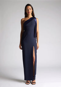 Front image of a model wearing a  One Shoulder Navy Maxi Dress with a  one shoulder contrast satin band and bow detail with a front skirt split. The design features Vesper Olympia One Shoulder Navy Maxi Dress