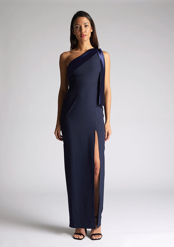 Front image of a model wearing a  One Shoulder Navy Maxi Dress with a  one shoulder contrast satin band and bow detail with a front skirt split. The design features Vesper Olympia One Shoulder Navy Maxi Dress