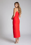 Back quarter image of blonde model wearing a red midaxi dress with a plunge neckline, delicate thin straps for a feminine touch, and front split that adds a modern edge. The design featured is the Vesper Palmer Red Midaxi Dress 
