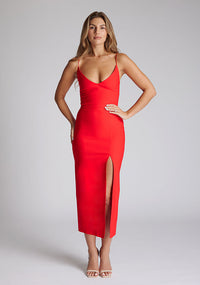Front image of blonde model wearing a red midaxi dress with a plunge neckline, delicate thin straps for a feminine touch, and front split that adds a modern edge. The design featured is the Vesper Palmer Red Midaxi Dress 