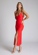 Front quarter image of blonde model wearing a red midaxi dress with a plunge neckline, delicate thin straps for a feminine touch, and front split that adds a modern edge. The design featured is the Vesper Palmer Red Midaxi Dress 