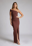 Front image of a blonde 
model wearing a  Chocolate Maxi Dress with an asymmetric neckline and one-sleeve design and front skirt split adds allure. The design features Vesper Pearson Chocolate Bardot Maxi Dress