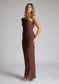 Front quarter image of a blonde 
model wearing a  Chocolate Maxi Dress with an asymmetric neckline and one-sleeve design and front skirt split adds allure. The design features Vesper Pearson Chocolate Bardot Maxi Dress