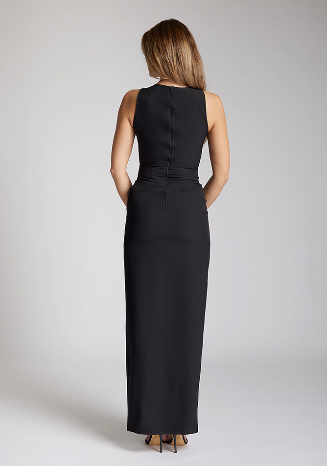 Back image of blonde model wearing a black asymmetrical detail maxi dress with a bold asymmetric neckline, front leg split and center back zip fastening. The design featured is the Vesper Polly Black Asymmetrical Detail Maxi Dress