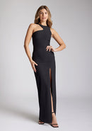 Front image of blonde model wearing a black asymmetrical detail maxi dress with a bold asymmetric neckline, front leg split and center back zip fastening. The design featured is the Vesper Polly Black Asymmetrical Detail Maxi Dress