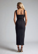 Back image of a model wearing a black midaxi dress with a sweetheart neckline with wide straps, a side cut-out and front skirt split. The design featured is the Vesper Porticini Black Cut Out Midaxi Dress