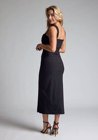 Back qaurter image of a model wearing a black midaxi dress with a sweetheart neckline with wide straps, a side cut-out and front skirt split. The design featured is the Vesper Porticini Black Cut Out Midaxi Dress